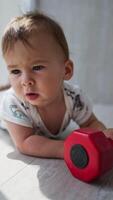 Lovely cute baby lying on the floor near the big window. Sweet toddler touching the red dumbbell. Blurred backdrop. Vertical video