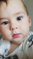 Cute kid with big grey eyes and sweet cheeks. Curious baby trying to reach the camera with his hand. Close up. Blurred backdrop. Vertical video
