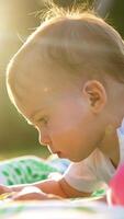 Half a year old baby lies on the ground in sun beams in summer. Kid interest in a toy moves it closer. Side view. Vertical video