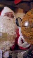 Santa Claus with globe in room. Santa Claus at his home making plans of travelling around the planet Vertical video