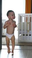 Smiling Caucasian baby in diaper running up to camera. Lovely kid being active at home. Vertical video