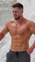 Man showing her perfect abs. Well built bodybuilder posing in the mountains Vertical video