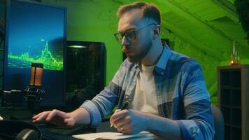 Focused serious Caucasian man freelancer male modern guy working writing results programmer crypto analyst typing keyboard computer pc concentration e-commerce home neon night trading stock deadline video