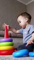 Boy in grey t-shirt plays with pyramid on the floor. Child breaks the pyramid. Low angle view. Vertical video