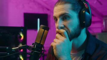 Pensive Caucasian man radio streamer speaking discussing microphone gamer male guy broadcasting game at home blogger vlogger pondering connection communication computer cyber sport pink light video