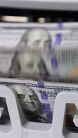 One hundred dollar wad being calculated in money counting machine. Benjamin Franklin portrait on the notes close up. Vertical video