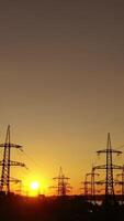 Sunset among high voltage towers. Transmission lines on the setting sun background. Electricity distribution in the evening. Motion camera back. Vertical video