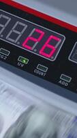 Numbers growing quickly on the display of cash counting machine. American dollars being counted in equipment. Close up. Vertical video