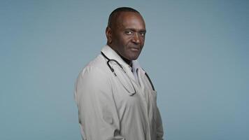 African american man doctor male physician turning to camera smiling inviting making gesture of invitation invite professional medical clinical service hospital advertisement in studio blue background video