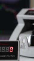 Bill counter screen with red numbers growing quickly. Hand puts US dollars into machine to count at backdrop in blur. Vertical video
