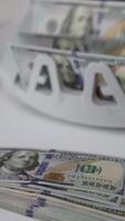 One hundred dollar banknotes on the table and in the cash counting machine. Male hand takes a wad of money showing them to the camera. Close up. Vertical video