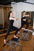 Two girls doing Pilates on a Pilates chair in a Pilates gym. A beautiful slim woman in black clothes performs exercises to strengthen the spine and leg muscles photo
