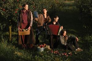 Four fashionable country girls at the apple harvest in the orchard. Happy girls playing accordion after apple harvest in an autumn orchard photo