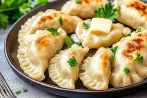 Delicious pierogi arranged in a circle on a dark plate with melted butter and parsley, served with a fork photo