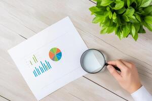 A businessman reviews financial charts and graphs with a magnifying glass in a modern workspace photo
