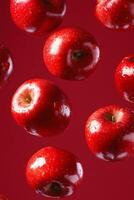 Bright red apples float mid-air against a deep red backdrop, showcasing their vivid color and glossy texture photo