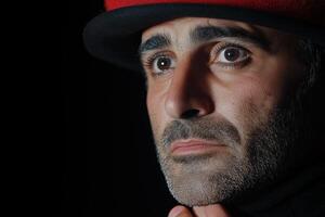 A sad clown holding his hand over his heart against a dark backdrop with focused lighting highlighting his emotions photo