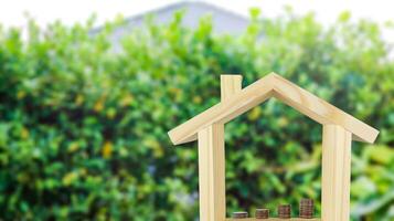 A wooden house model with coins arranged in ascending order inside, set against a blurred background of bushes, symbolizing financial growth and investment for home ownership. photo