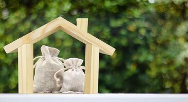 Wooden house model with burlap sacks of coins arranged inside, representing the idea of saving money to build or invest in a home. photo