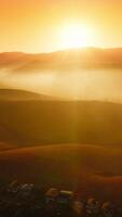 Beautiful hills in the bright rays of sun hiding behind the mountain. Drone flight over the city locating in the mountainous territory. Aerial view. Vertical video