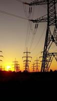 Transmission electric on towers at sunset. High-voltage power lines. Electrical pylons on the orange sky background. Drone view. Camera rising up. Vertical video