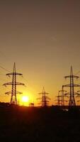 Electric power station in the evening. High voltage electric lines against the setting sun. Transmission lines. Motion camera back. Vertical video