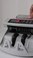 Little money counting machine turning money. Laptop with a black screen and a curve at backdrop in blur. Vertical video