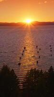 Yachts and boats holding still on the waters of amazing lake in the rays of setting sun. Mountainous horizon and orange sky at backdrop. Vertical video