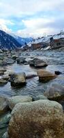 A river with rocks and snow covered mountains in the background photo