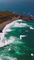 Sunny scenery of Morro Bay rocky coastline at daytime. Low white waves coming to the narrow line of a sandy beach. Top view. Vertical video