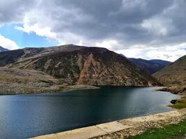 A lake surrounded by mountains and a road photo