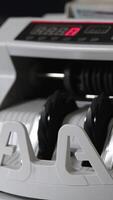 White compact cash counting machine working. One hundred dollar bills being turned in the counter. Close up. Vertical video