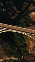 Rising over the bridge with two-lane road for cars. Top view on the gap between the mountains with vegetation growing abundantly there. Vertical video