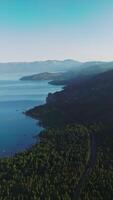 Wonderful scenery of mountainous landscape covered with pine trees. Beautiful peaceful lake with some mist over it in the foot of the mountains. Aerial view. Vertical video