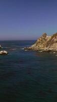 Flying low over the deep blue water of ocean. Approaching the passage between two rocks with algae on the water surface. Vertical video