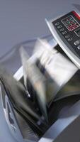 Man puts a big wad of hundred dollar notes into money counting machine. Side view. White background. Vertical video