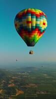 Bright colorful hot air balloon descending in the blue sky. Aerostats soaring over the hazy mountains on sunny day. Top view. Vertical video