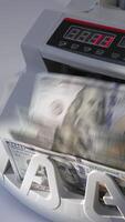 Male puts a wad of US dollars into money machine. Equipment for financial operations working. High angle view. Close up. Vertical video