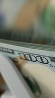 New hundred dollar bills quickly falling on the holder of machine. Close up. Financial equipment at work. Blurred backdrop. Vertical video