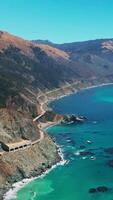 Breath-taking scenery of mountains with some greenery growing on. Turquoise ocean washing the rocky shore. Aerial view. Vertical video
