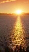 Sailing boats on the surface of beautiful lake. Lake Tahoe, California, USA in the rays of sun setting behind the mountains. Top view. Vertical video