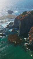 Flying closer to the mansion locating on the tor of the rocks at California coastline. Pacific ocean splashing waves by the rugged shore. Aerial view. Vertical video