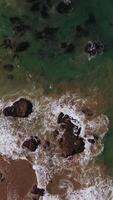 Lovely pleasant view of foamy waves splashing by the rocks at the shore. Beautiful sight of sea water sparkling in the sun from aerial perspective. Vertical video