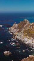 Rocks overgrown with moss surrounded by blue deep waters. Stunning seascape with hazy line of horizon on sunny day. Vertical video