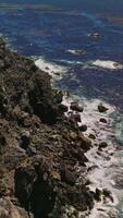 Flight over the cliff on the coastline of Pacific ocean. Some grass and moss covering the shore. Houses and roads on the top of mountains. Vertical video