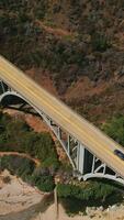 Mountains connected by the arch bridge with cars moving by. Drone descending above the rocks covered with moss. Vertical video