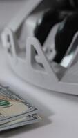 Lots of hundred dollar bills are calculated in the money machine. A wad of American dollars lies in front of equipment. Close up. Blurred backdrop. Vertical video