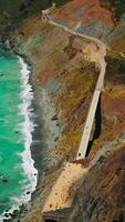 Flight over the highway in the sloping mountains of California coast. Beautiful azure ocean splashing by the rocks. Aerial view. Vertical video