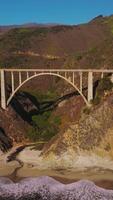 Arched bridge over the gap between the mountains. Sunlit mountains of California in the bright rays of sun. Aerial perspective. Vertical video