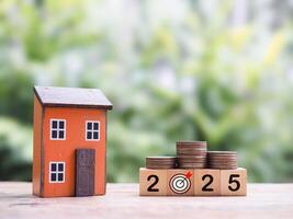 Miniature house, Wooden blocks with the number 2025 and stack of coins. The concept of saving money for house, Property investment, House mortgage, Real estate in year 2025 photo